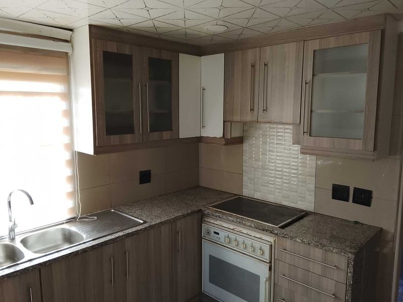 A functional kitchen featuring wood-look laminate cabinetry, granite countertops, a built-in oven with hob, and a double sink with tiled backsplash.
