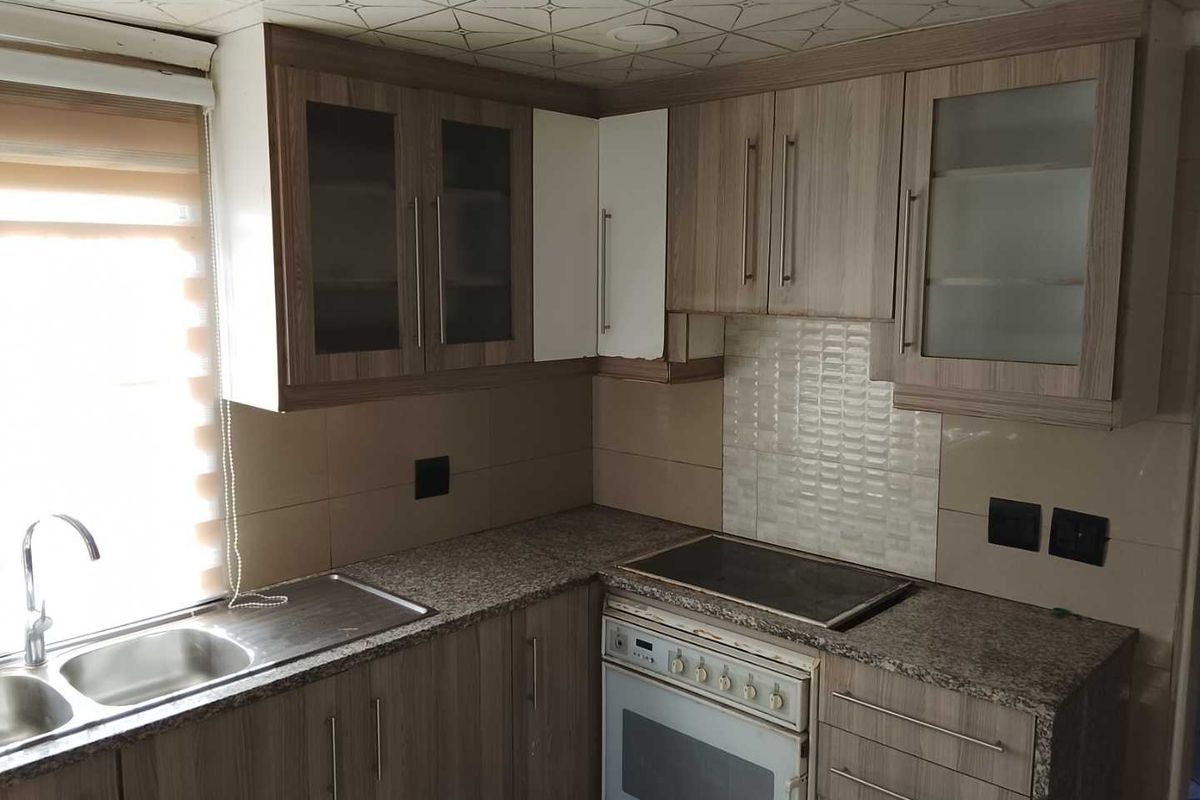 A functional kitchen featuring wood-look laminate cabinetry, granite countertops, a built-in oven with hob, and a double sink with tiled backsplash.