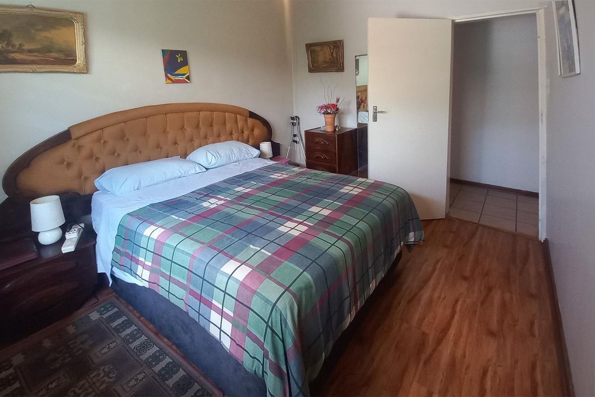 A bedroom featuring wood-look laminate flooring and a standard interior door leading to an adjacent tiled space.