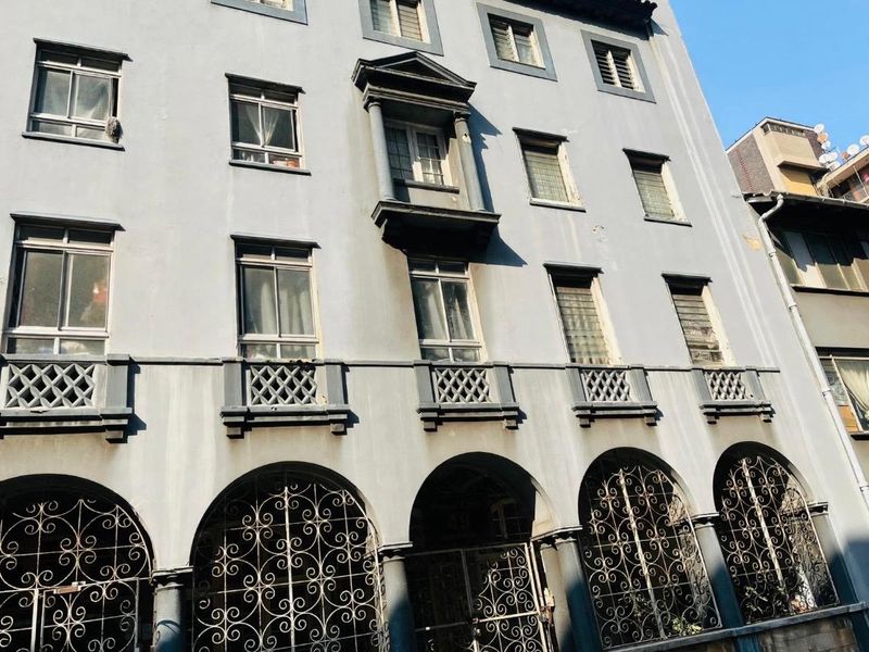 A multi-story apartment building facade featuring arched ground floor security grilles, decorative balcony balustrades, and a prominent central window bay.