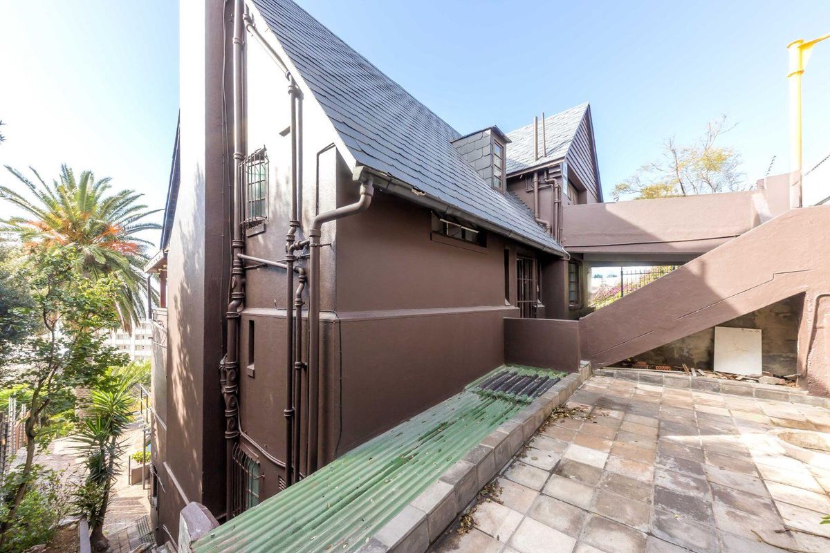 Side exterior view of the property featuring a multi-level facade, slate roof, external staircase, and paved terrace area.