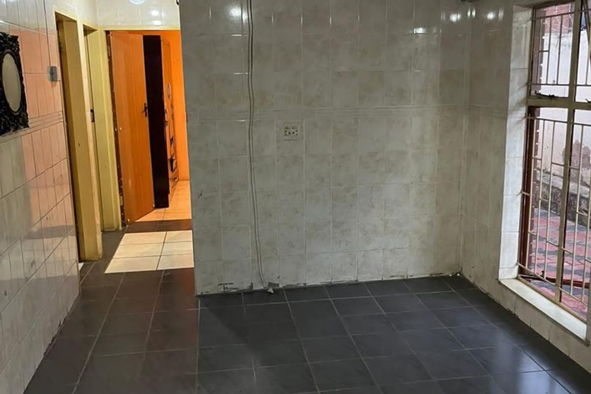 An interior space featuring tiled walls and dark floor tiles, with a window overlooking an exterior area and access to an adjacent hallway.