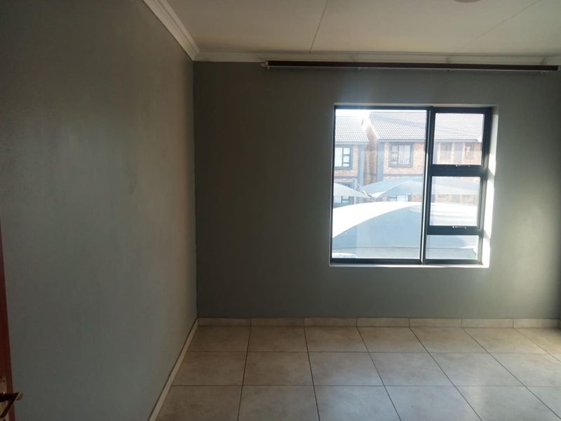 An empty bedroom featuring neutral grey walls, tiled flooring, and an aluminium window frame with a curtain rail.