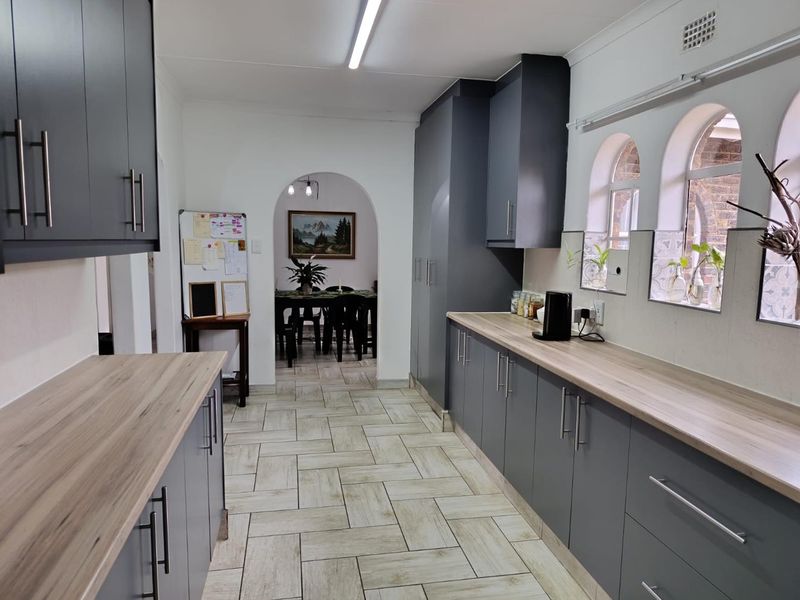 Modern kitchen featuring grey cabinetry, light wood-look laminate countertops, tiled flooring, and an arched entryway leading to the dining area.