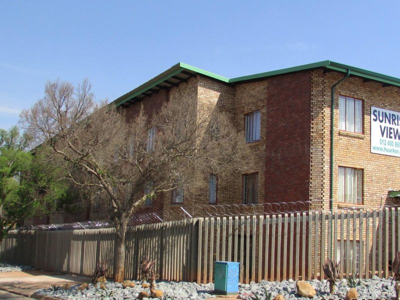 Exterior view of a multi-story face brick apartment building featuring secure perimeter fencing and prominent signage.