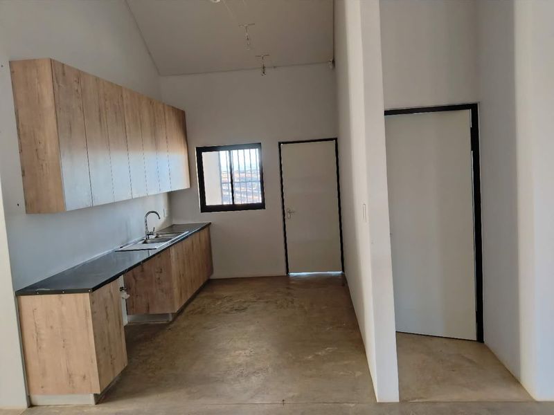A functional kitchen area featuring modern wood-look cabinetry, dark countertops, and a stainless steel sink, set within an open-plan space with concrete flooring.