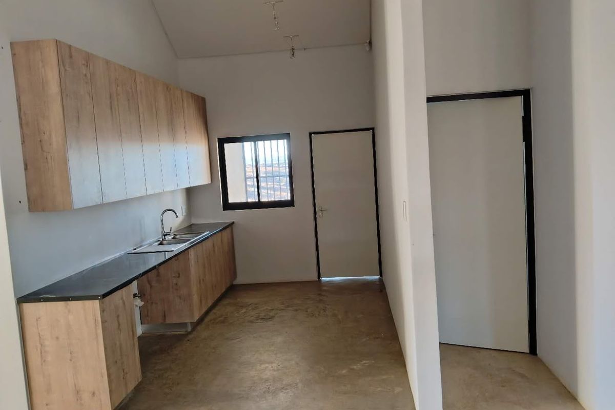 A functional kitchen area featuring modern wood-look cabinetry, dark countertops, and a stainless steel sink, set within an open-plan space with concrete flooring.