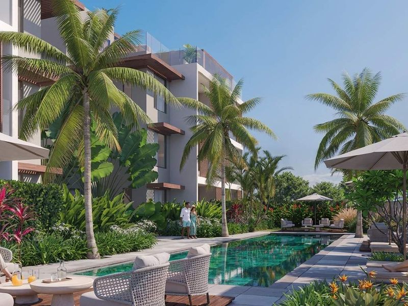 A beautifully landscaped outdoor pool area featuring a modern swimming pool, stone decking, and lush tropical gardens set against a contemporary apartment building.