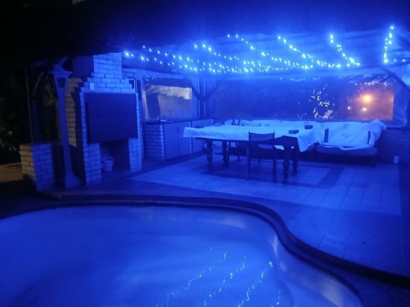 Outdoor entertainment area featuring a swimming pool, covered patio with a built-in braai, and overhead lighting.