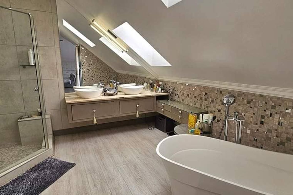 Modern attic bathroom featuring a freestanding bathtub, glass-enclosed shower, dual vessel sinks on a floating vanity, and skylights providing natural light.
