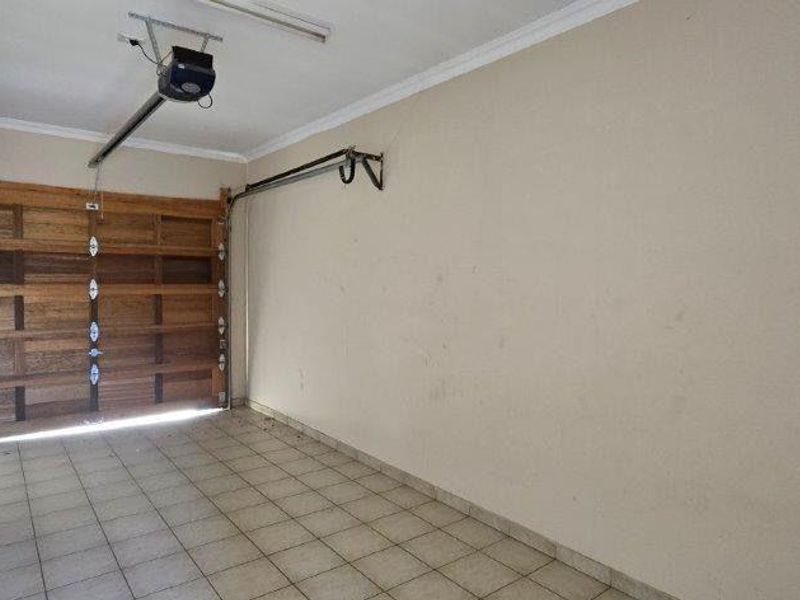 A clean, empty garage featuring tiled flooring and a wooden sectional garage door with an automated motor.