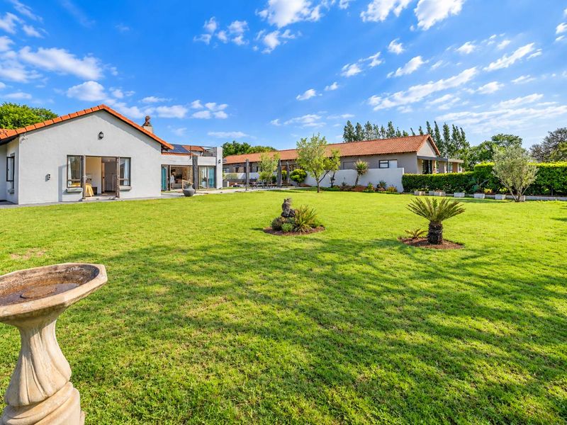 Spacious rear garden featuring a well-maintained lawn, mature landscaping, and a view of the rear building elevation with terracotta roof tiles.