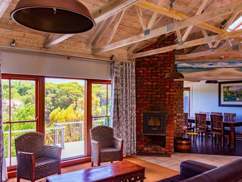 Spacious open-plan living area featuring exposed timber roof trusses, a prominent brick fireplace with a wood-burning stove, and large windows overlooking the garden.