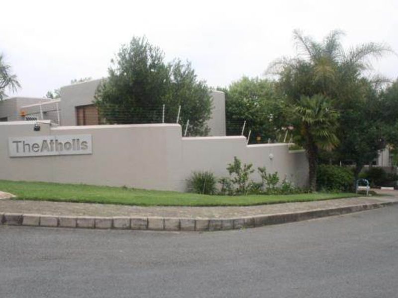 Street view of the apartment complex entrance featuring a perimeter wall with electric fencing and landscaped garden area.
