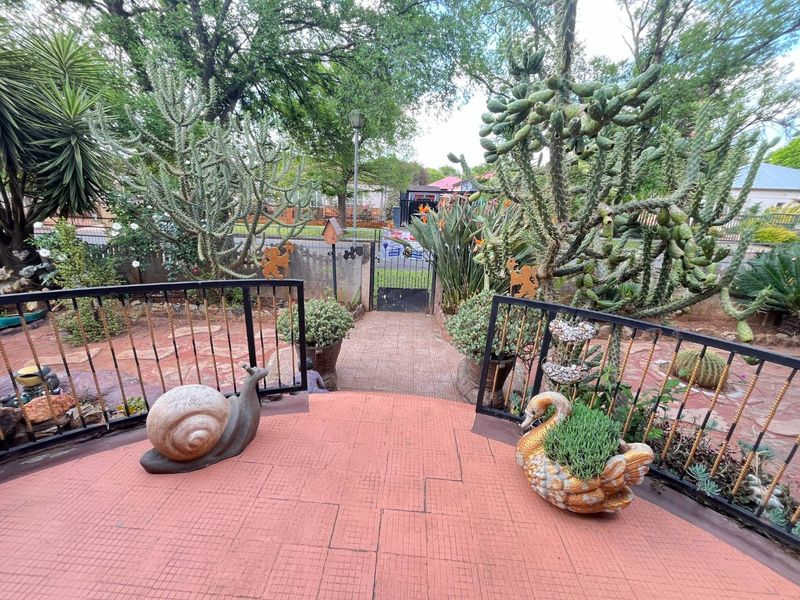 A landscaped garden area featuring a tiled patio, metal railings, and a paved walkway leading to a pedestrian gate.