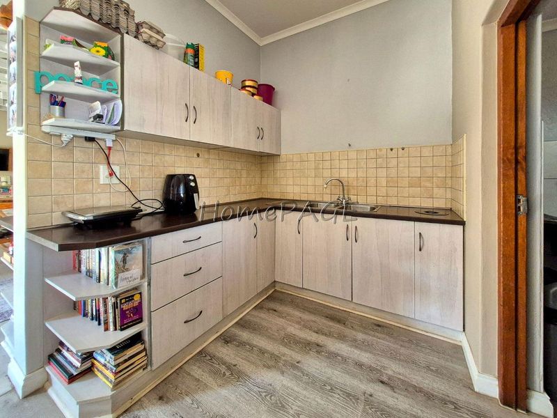A functional scullery area featuring laminate cabinetry, a stainless steel sink, tiled backsplash, and durable laminate flooring.
