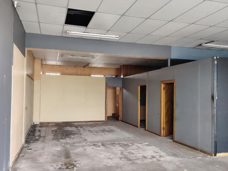 An empty, open-plan commercial space featuring a suspended ceiling, partition walls, and exposed flooring, requiring significant renovation and cosmetic updates.