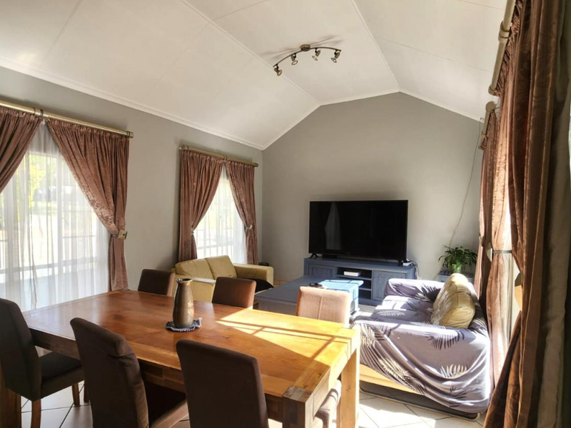 Spacious open-plan living and dining area featuring a high vaulted ceiling, tiled flooring, and large windows with curtain treatments.