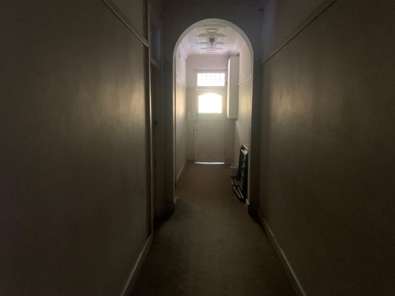 A narrow hallway featuring a classic archway and decorative ceiling, leading to an exterior entrance door with a transom window.
