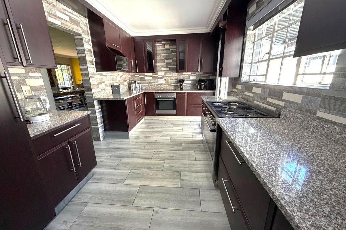A well-maintained kitchen featuring dark wood cabinetry, granite countertops, a gas hob, built-in oven, and modern stone-tiled backsplash and flooring.