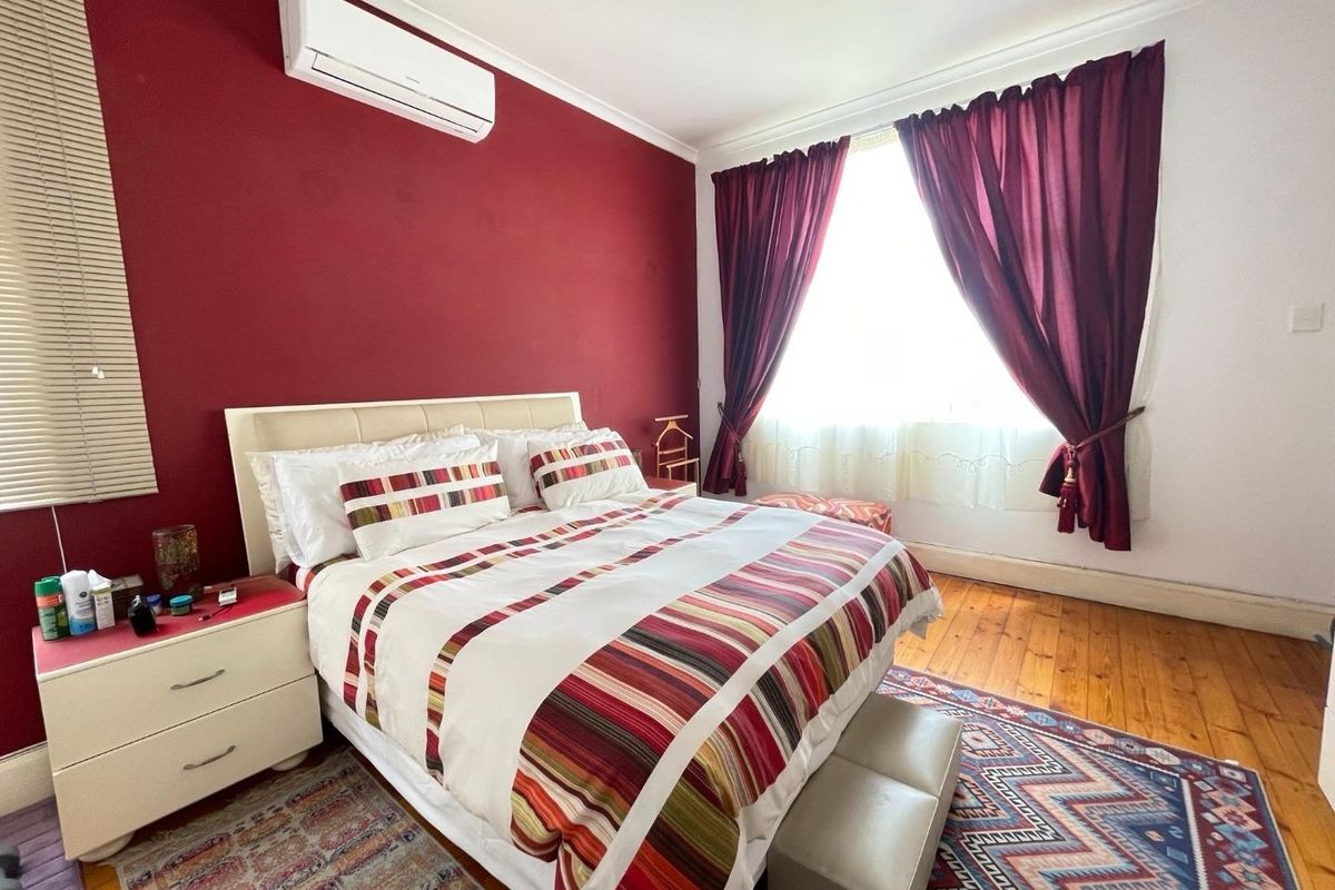 A bedroom featuring timber flooring, a wall-mounted split-system air conditioner, and a bold red accent wall.