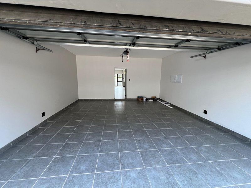 A clean, spacious double garage featuring tiled flooring, a sectional overhead door, and direct access into the main living area of the home.