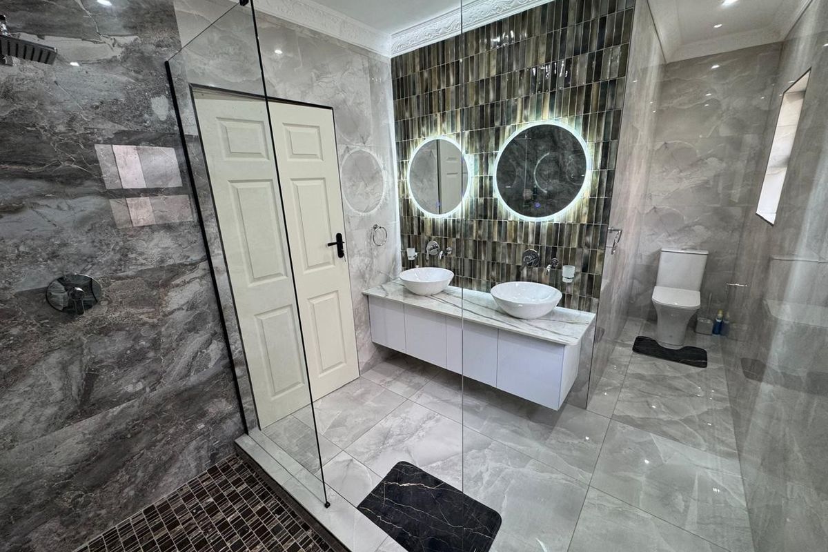 Modern, high-end bathroom featuring a double vanity with vessel sinks, backlit mirrors, a spacious walk-in shower with glass enclosure, and premium floor-to-ceiling tiling.