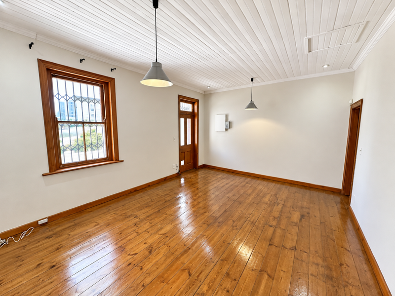 A bright, empty living room featuring polished timber flooring, a classic beaded timber ceiling, and natural light through a timber-framed window with security bars.