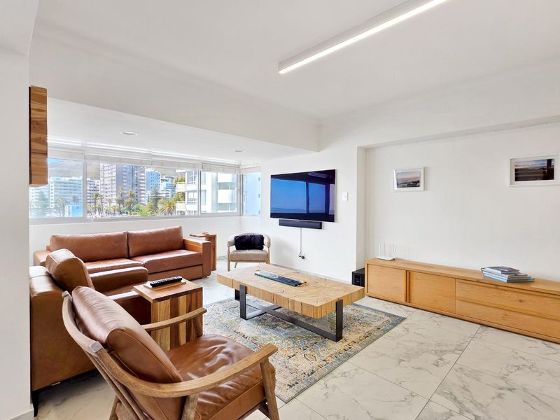 A bright and modern living room featuring large windows with city views, marble-look tiled flooring, and clean, minimalist finishes.