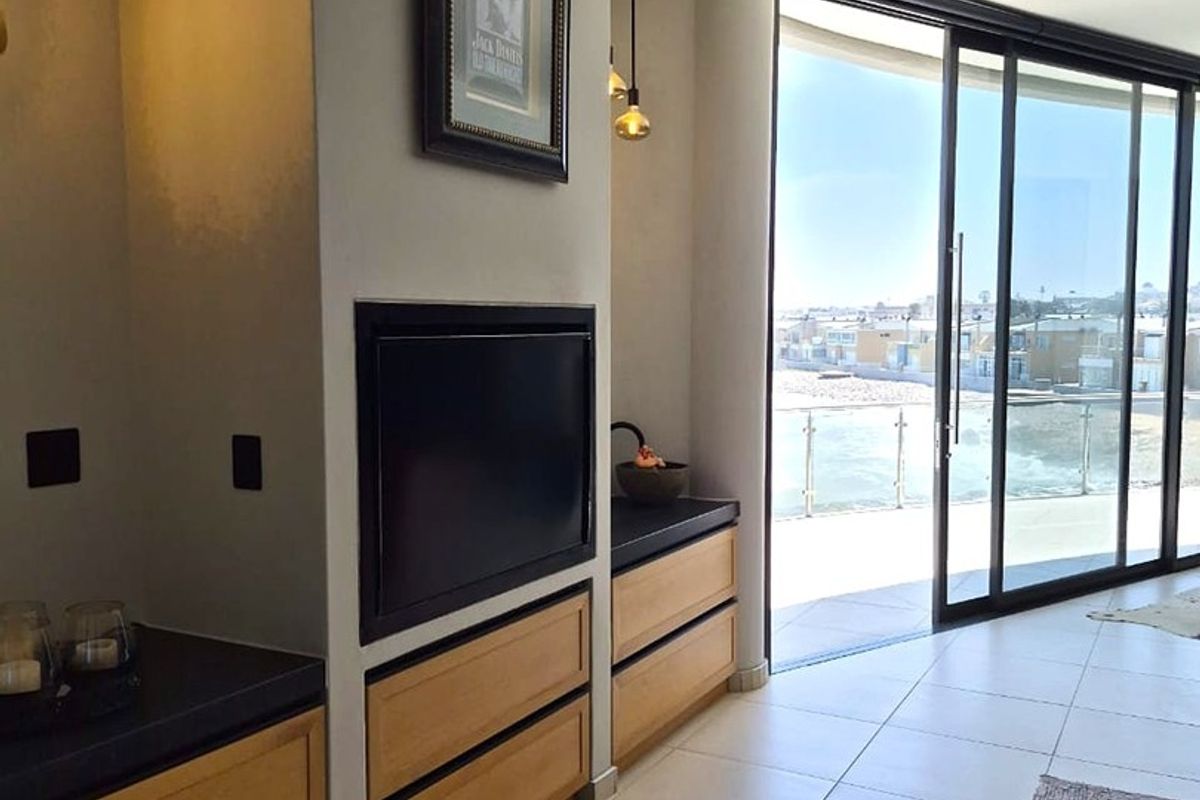 Modern living area featuring built-in wooden cabinetry, a sleek fireplace, and large sliding glass doors opening to a balcony with coastal views.