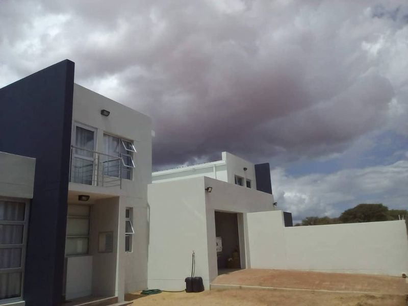 Modern two-story apartment exterior featuring a clean white and dark grey facade, balcony with stainless steel railing, and an integrated garage.