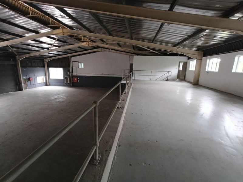 Spacious industrial warehouse interior featuring a mezzanine level, exposed steel roof structure, concrete flooring, and a large roller shutter door for easy access.