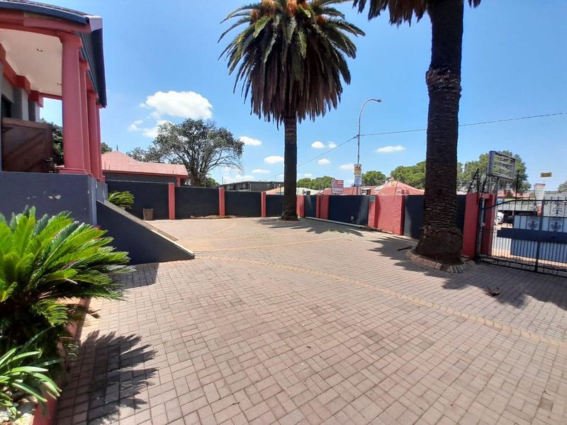 A paved front driveway area featuring a secure metal gate, boundary walls, and mature palm trees providing a clear entrance to the property.