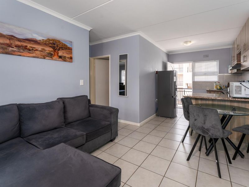 Open-plan living area featuring tiled floors, a functional kitchen with granite countertops, and a breakfast nook leading to a balcony.