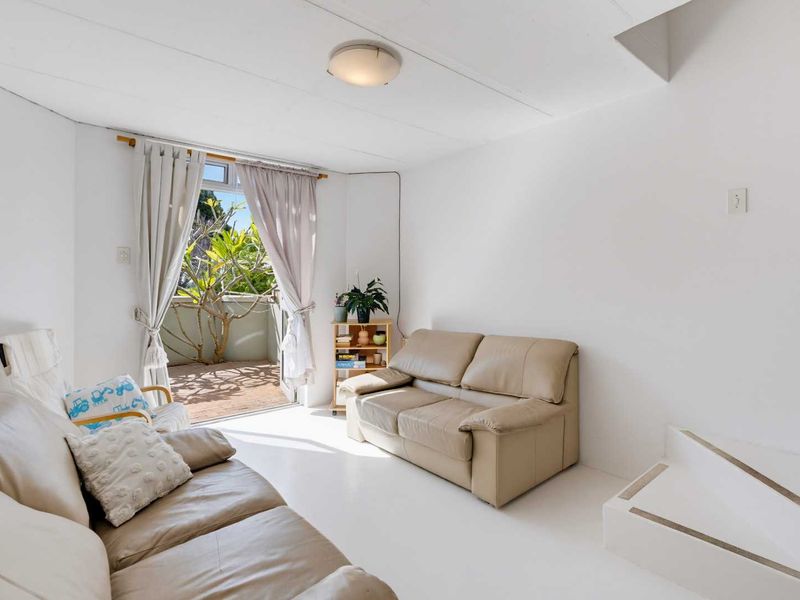 A bright living room featuring tiled flooring, a built-in step, and a sliding glass door providing access to an outdoor balcony area.
