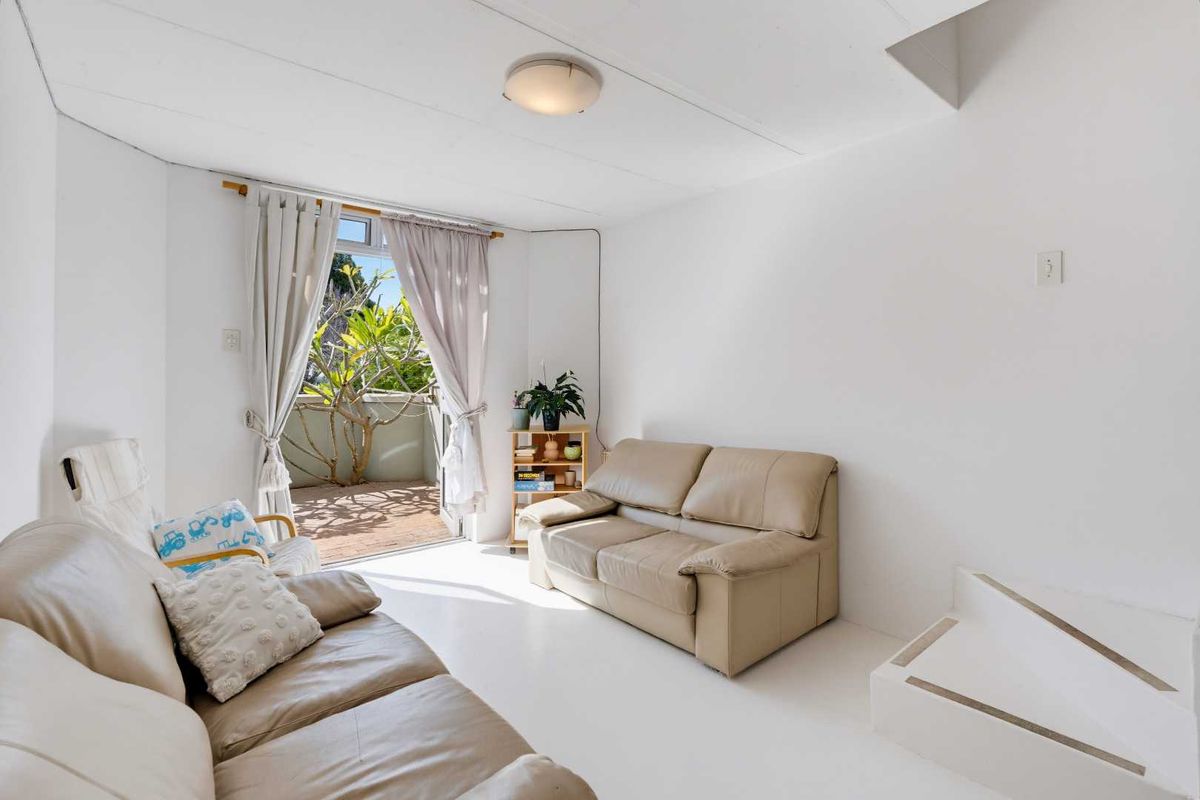 A bright living room featuring tiled flooring, a built-in step, and a sliding glass door providing access to an outdoor balcony area.