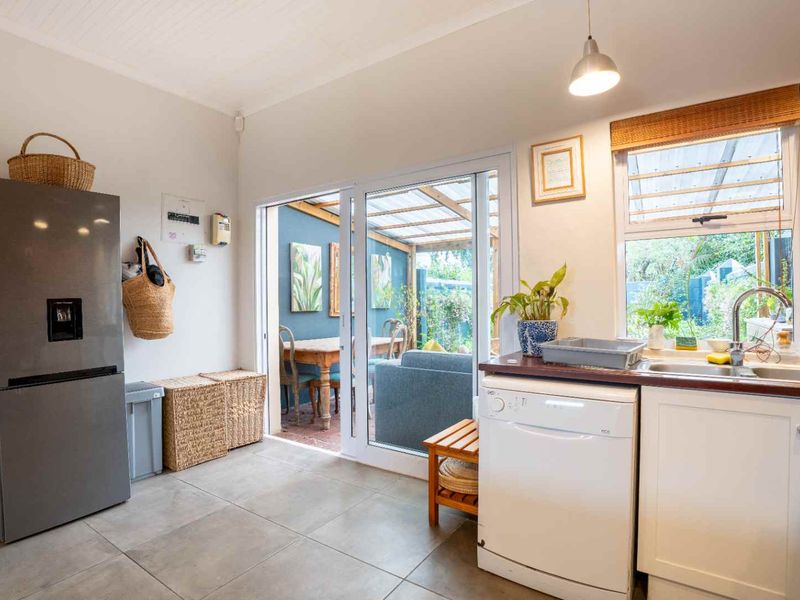 A bright kitchen featuring tiled flooring, a stainless steel sink, and direct access to an outdoor patio area through sliding glass doors.