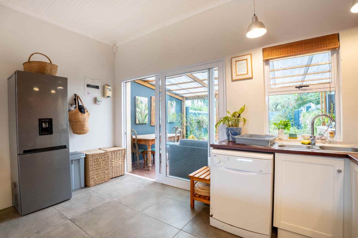 A bright kitchen featuring tiled flooring, a stainless steel sink, and direct access to an outdoor patio area through sliding glass doors.