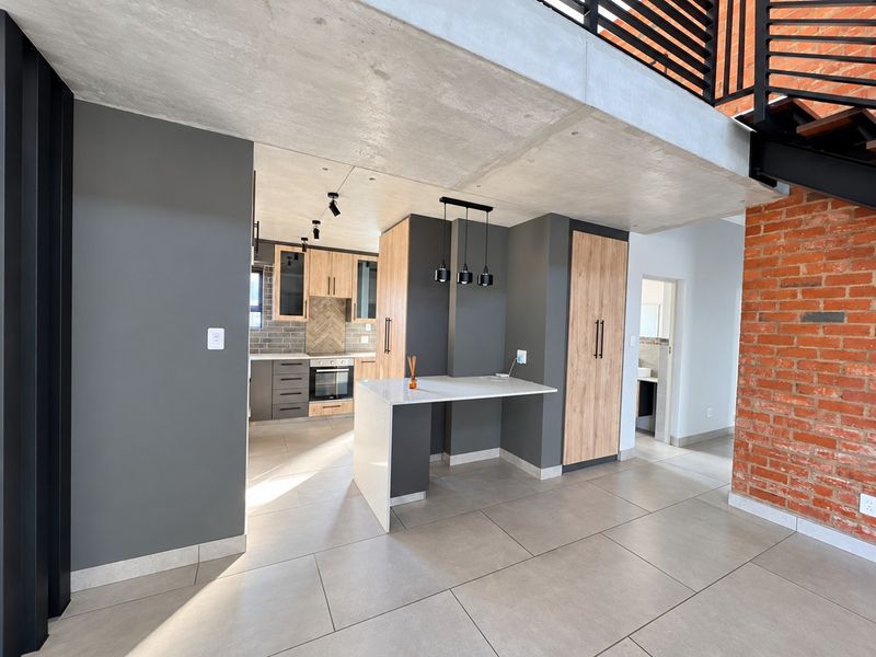 Modern open-plan kitchen featuring sleek cabinetry, built-in appliances, a central island, exposed concrete ceilings, and industrial-style brick accents.
