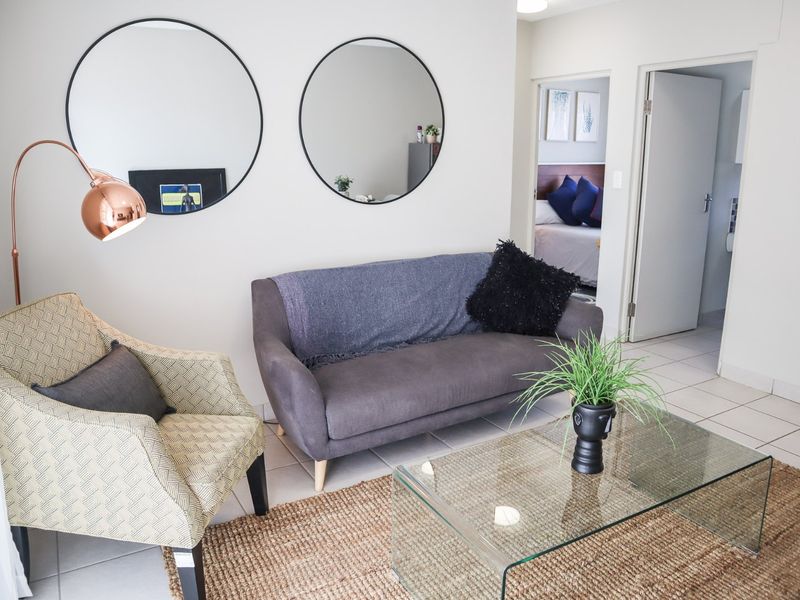 A bright living room area featuring neutral tiled flooring and access to an adjacent bedroom.