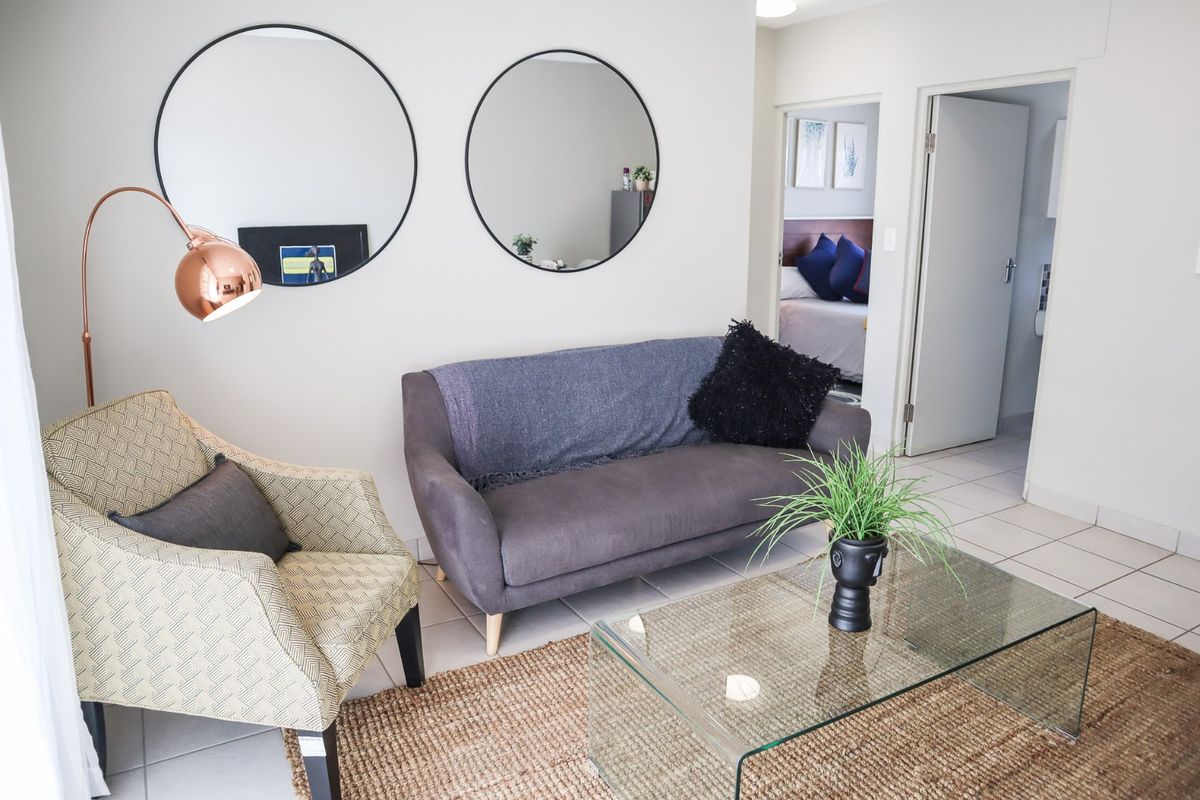 A bright living room area featuring neutral tiled flooring and access to an adjacent bedroom.