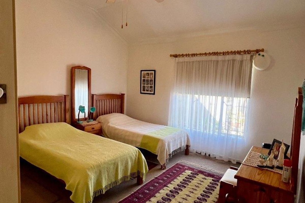 A bedroom featuring a vaulted ceiling, a central ceiling fan, and a large window with fitted curtain rod.