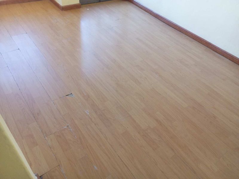 An empty living area featuring light-toned laminate flooring with visible wear and damage to the planks.
