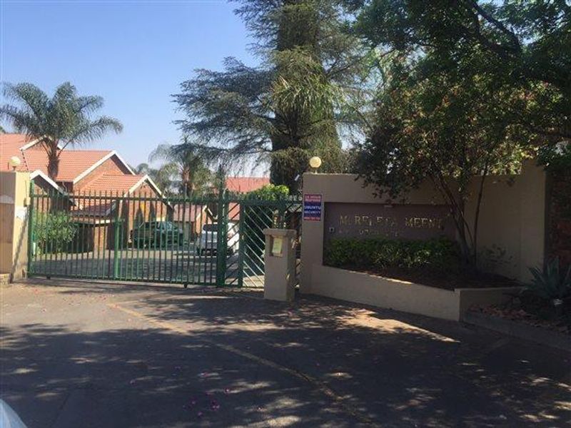 Entrance view of the townhouse complex featuring a secure gated access point and perimeter boundary wall.