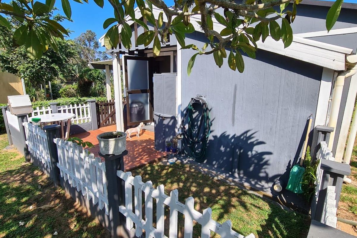 A rear exterior view of the property featuring a tiled patio area, white picket fencing, and timber-clad exterior walls.