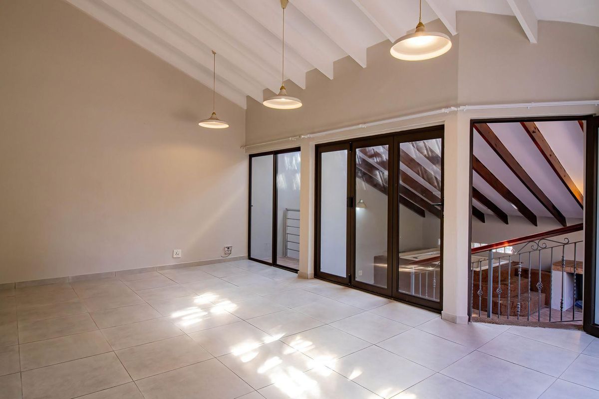 Spacious living area featuring vaulted ceilings with exposed beams, large glass sliding doors, and neutral tiled flooring.