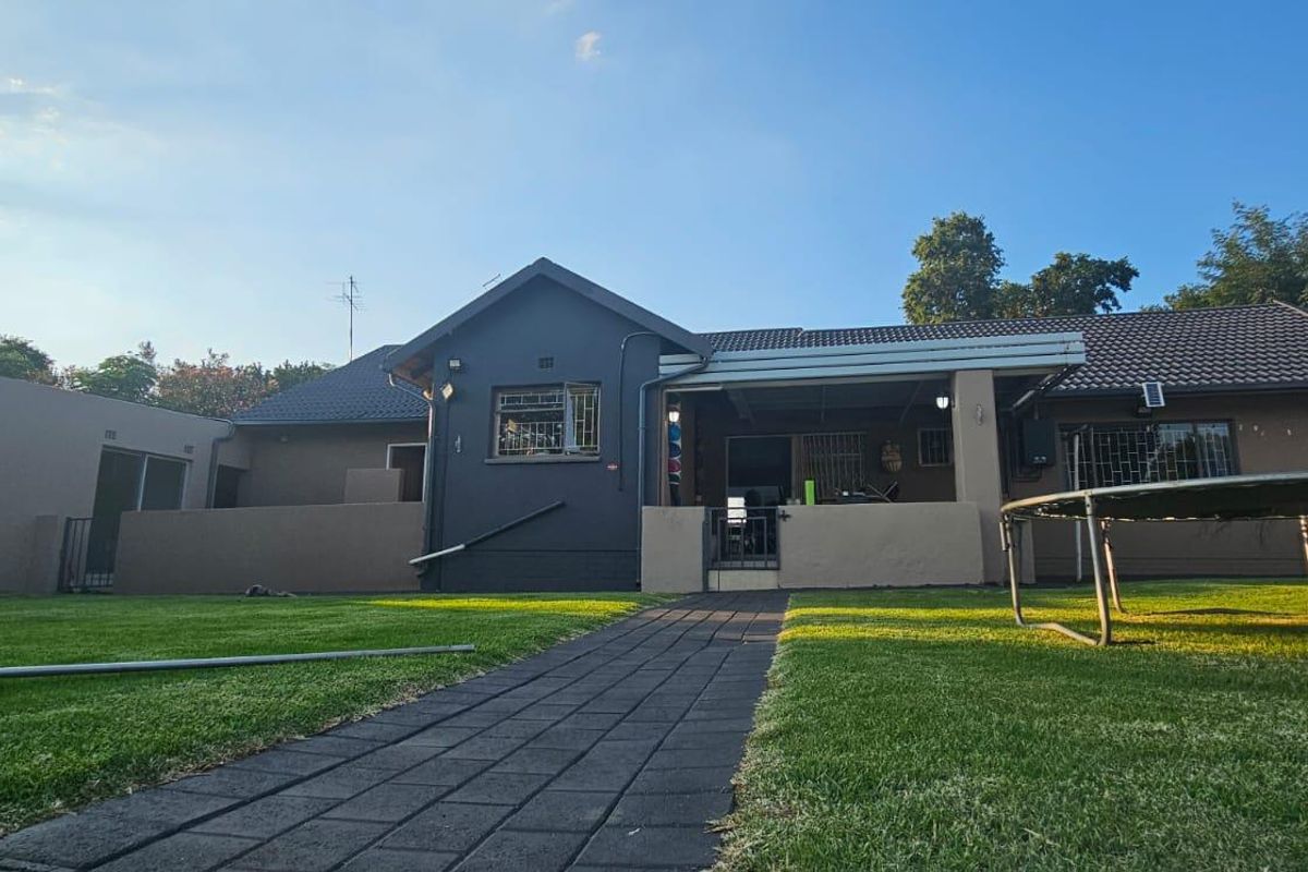 Rear view of the house featuring a paved walkway, well-maintained lawn, and a covered patio area.