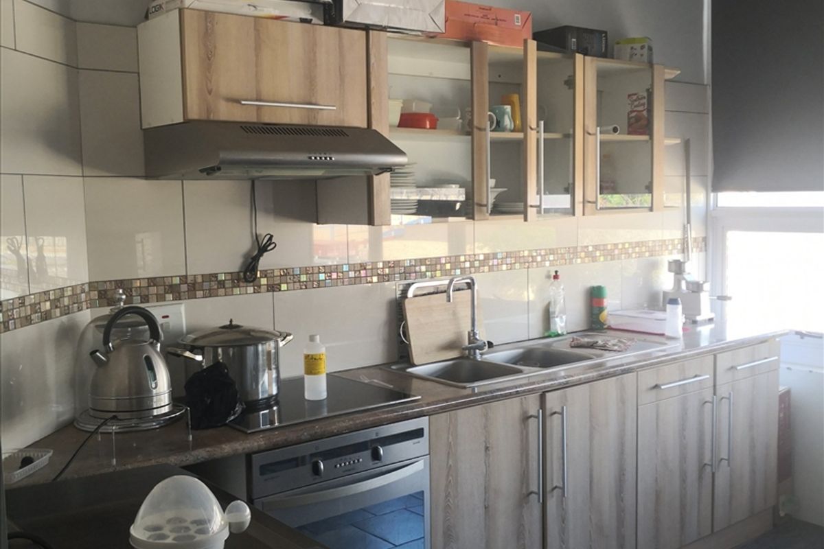 A functional kitchen featuring wood-look cabinetry, a built-in oven with extractor fan, double sink, and tiled backsplash with dark floor tiles.