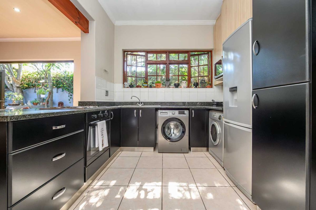A functional kitchen featuring dark cabinetry, granite countertops, integrated appliances, and a tiled floor, with a view looking out toward the garden.