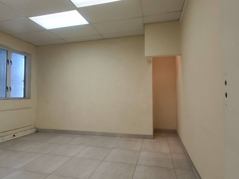 A vacant office space featuring tiled flooring, a suspended ceiling with recessed lighting, and a wall-mounted air conditioning unit.